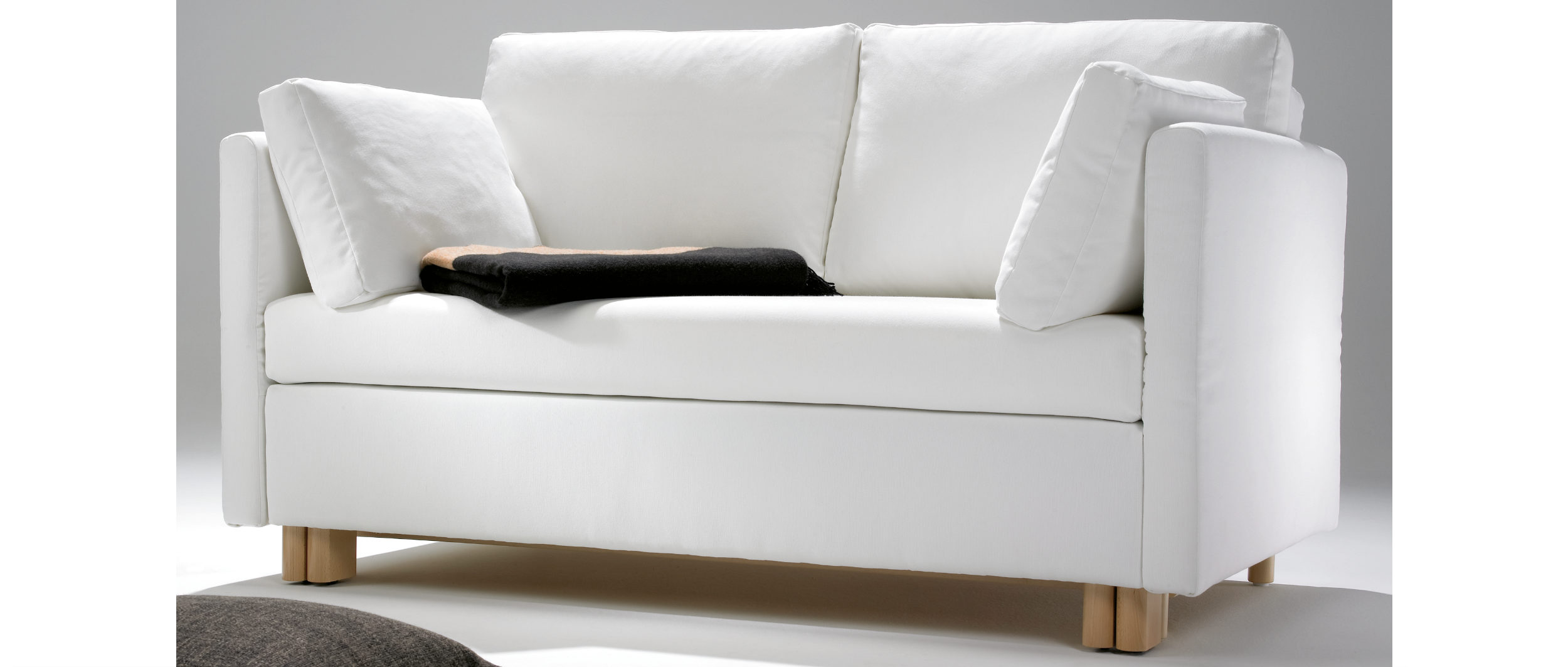 Das Schlafsofa PAULA in Leder mit Holzfüßen kombiniert.