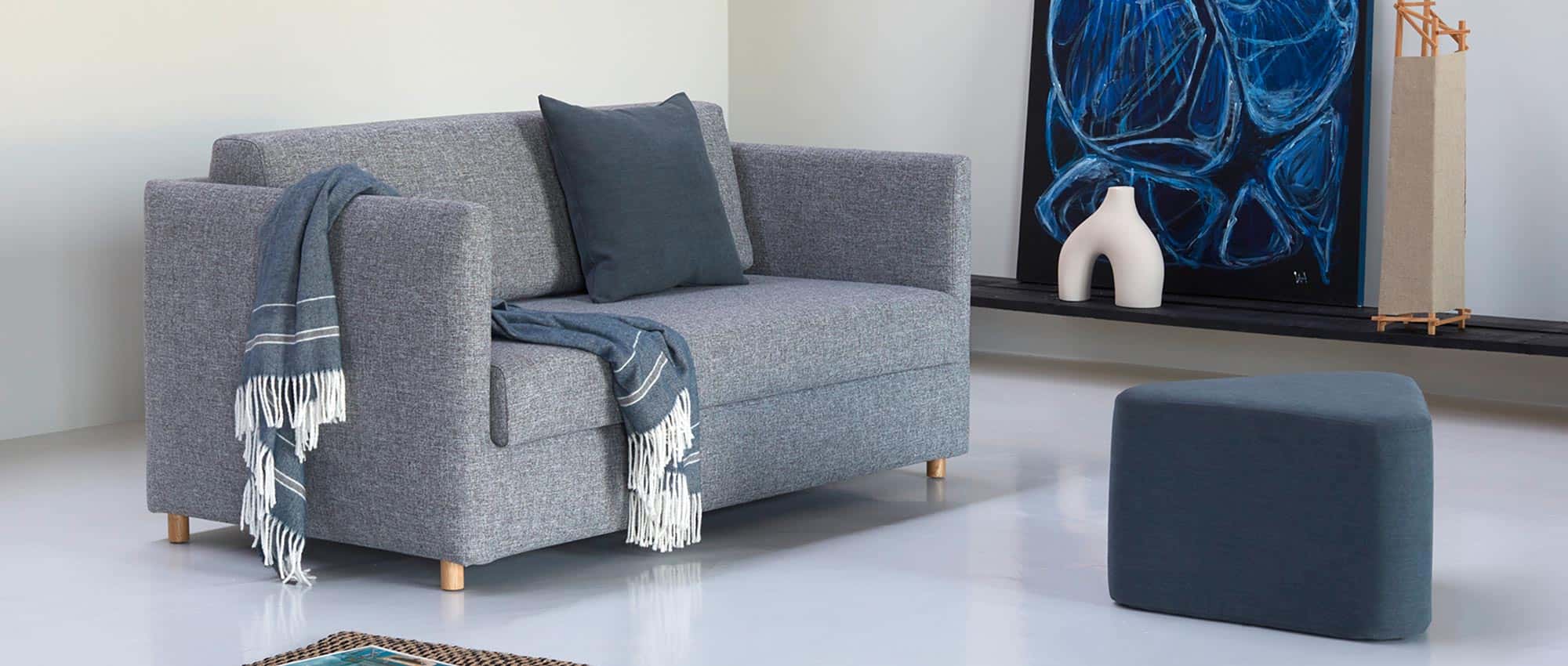 Das OLAN Schlafsofa von Innovation im Stoff Twist Granite (565) und mit dem TRIANGULAR Hocker kombiniert